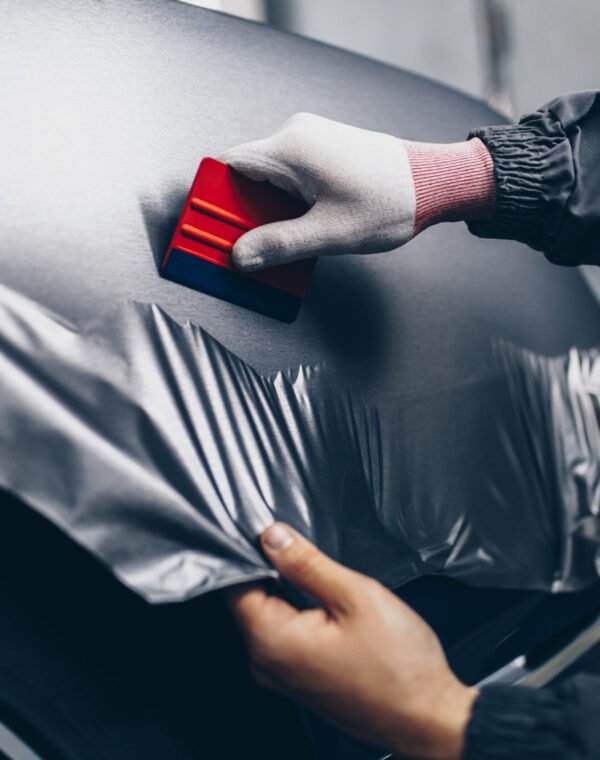 Car wrapping specialist putting vinyl foil or film on car. Selective focus.
